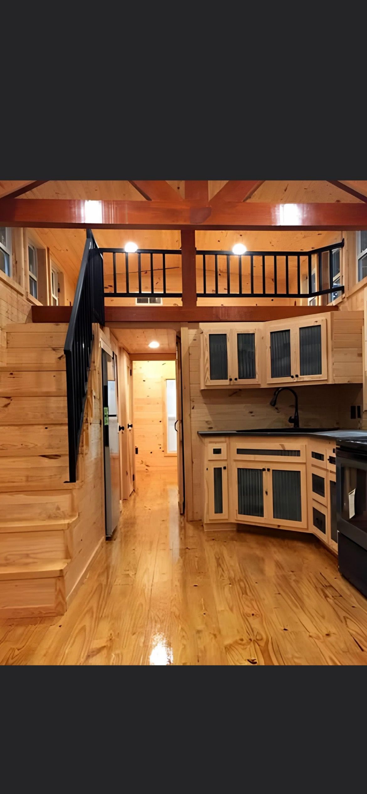 A kitchen with wooden cabinets and stairs leading to a loft.