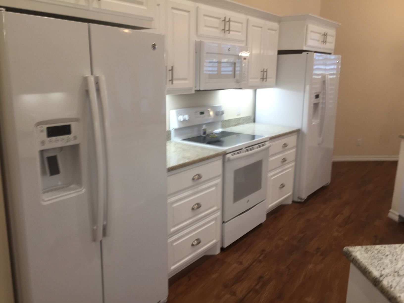 A kitchen with white cabinets and appliances including a refrigerator