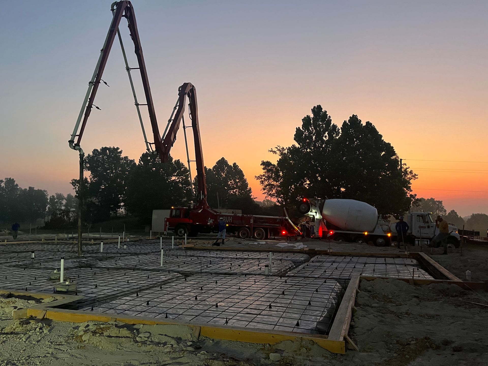 A concrete pump is being used on a construction site at sunset