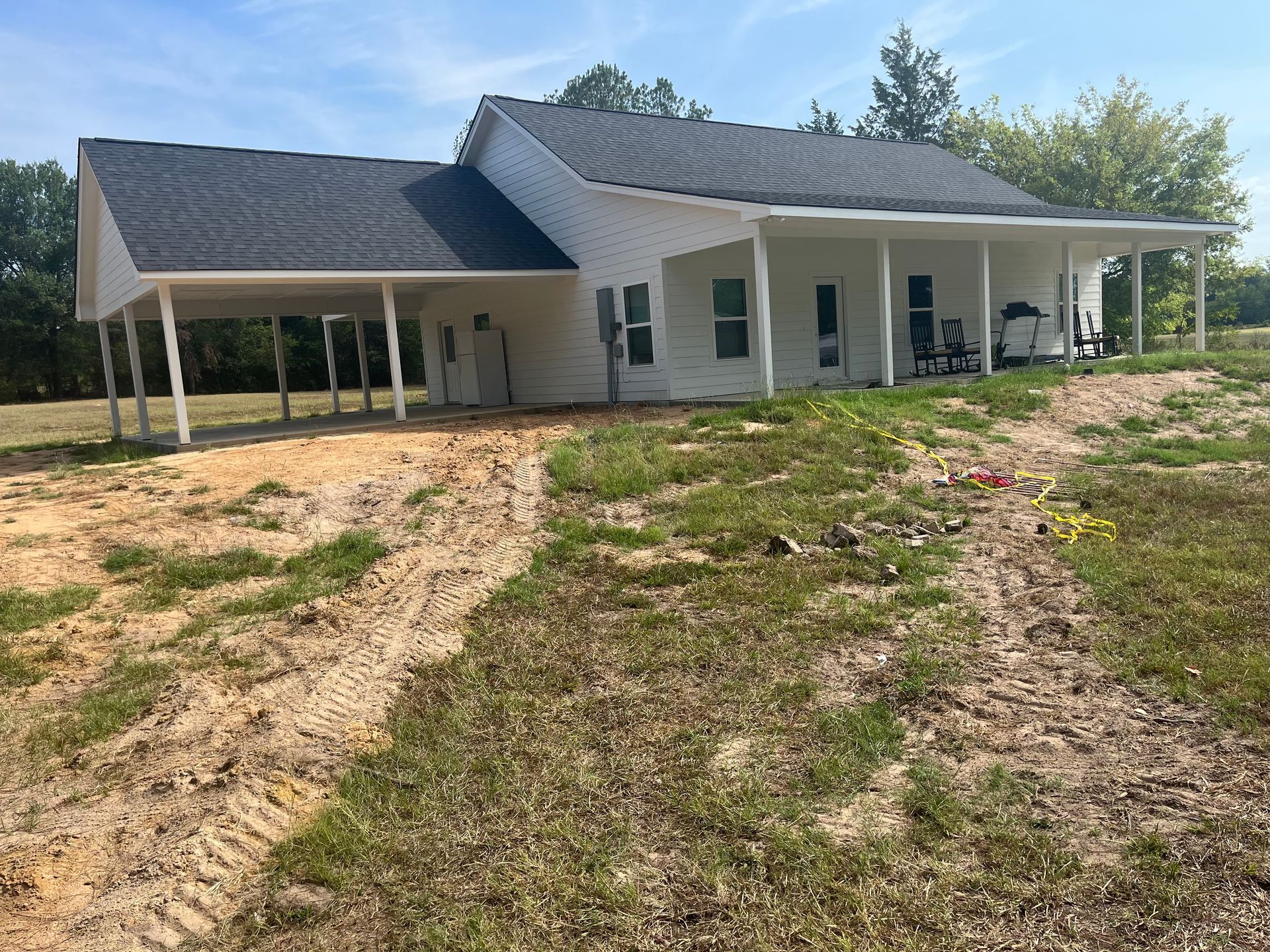 A white house with a porch is sitting on top of a dirt field.