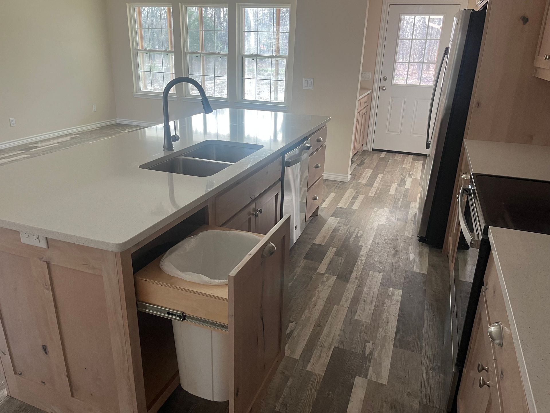 A kitchen with a sink and a trash can in it.