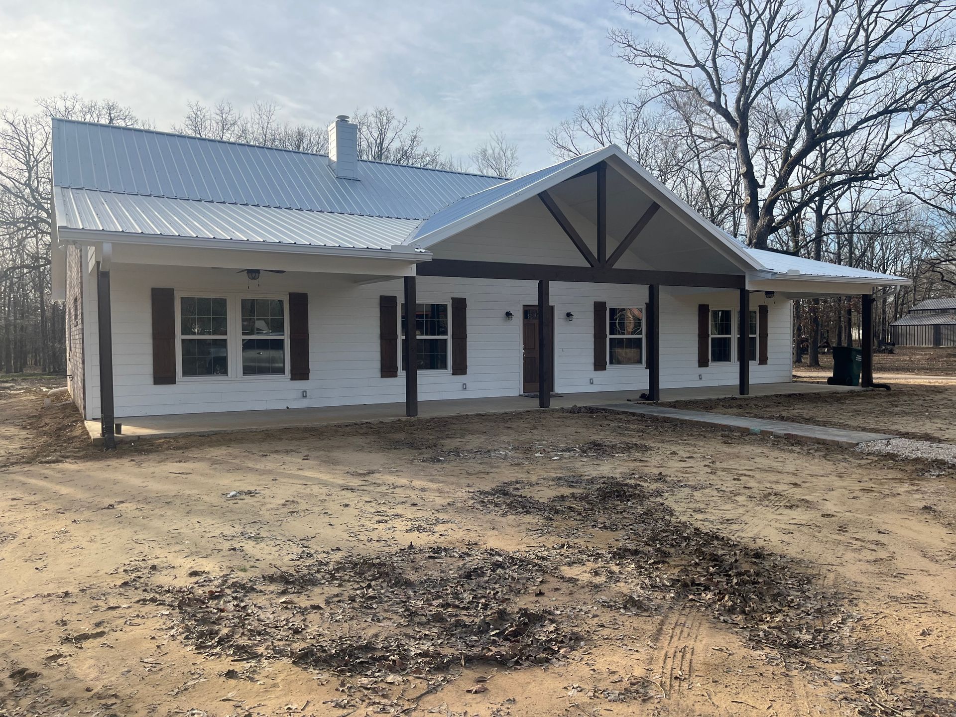 A white house with a metal roof and a porch in the middle of a dirt field.