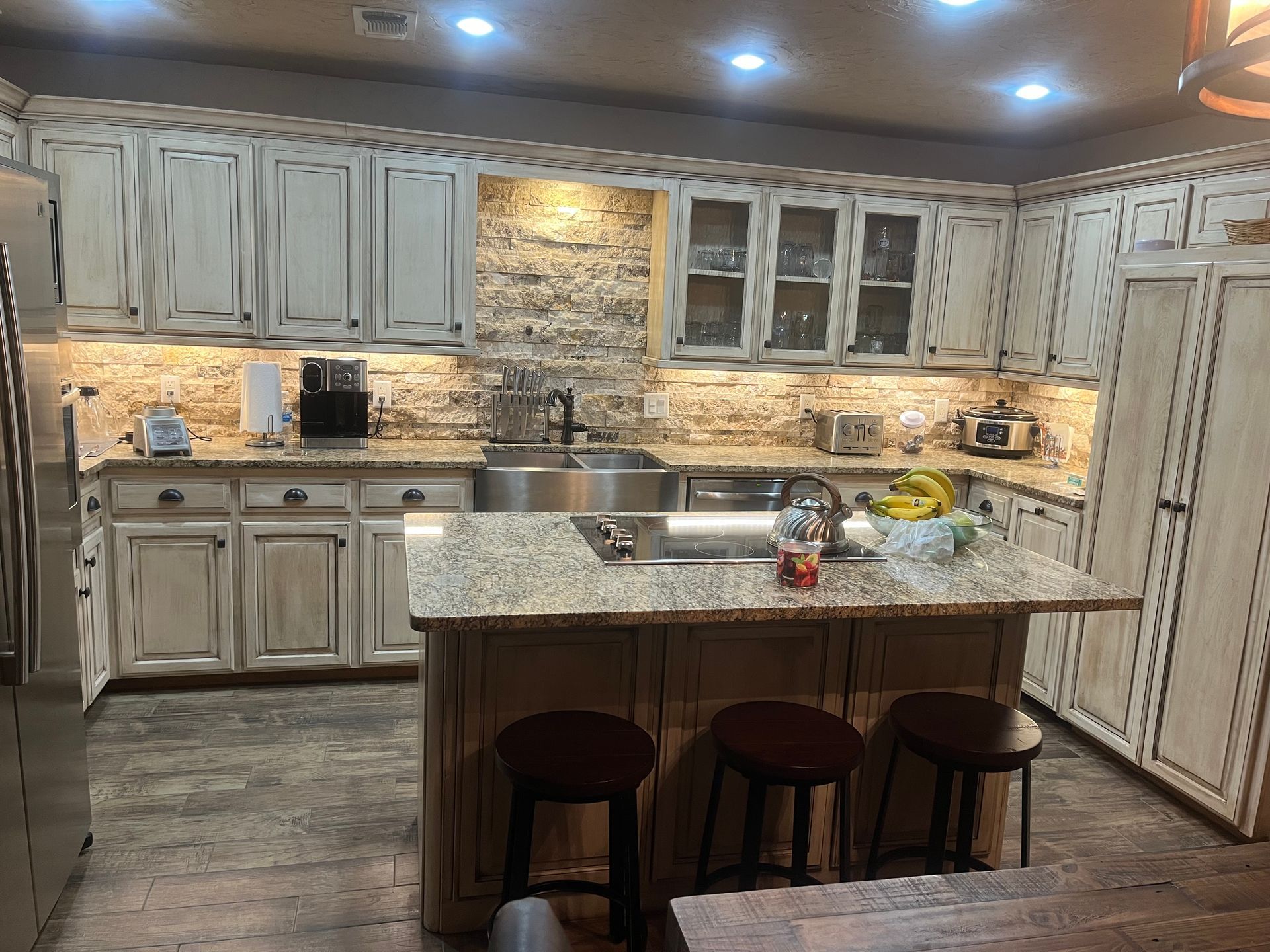 A kitchen with white cabinets , granite counter tops , stainless steel appliances and a large island.