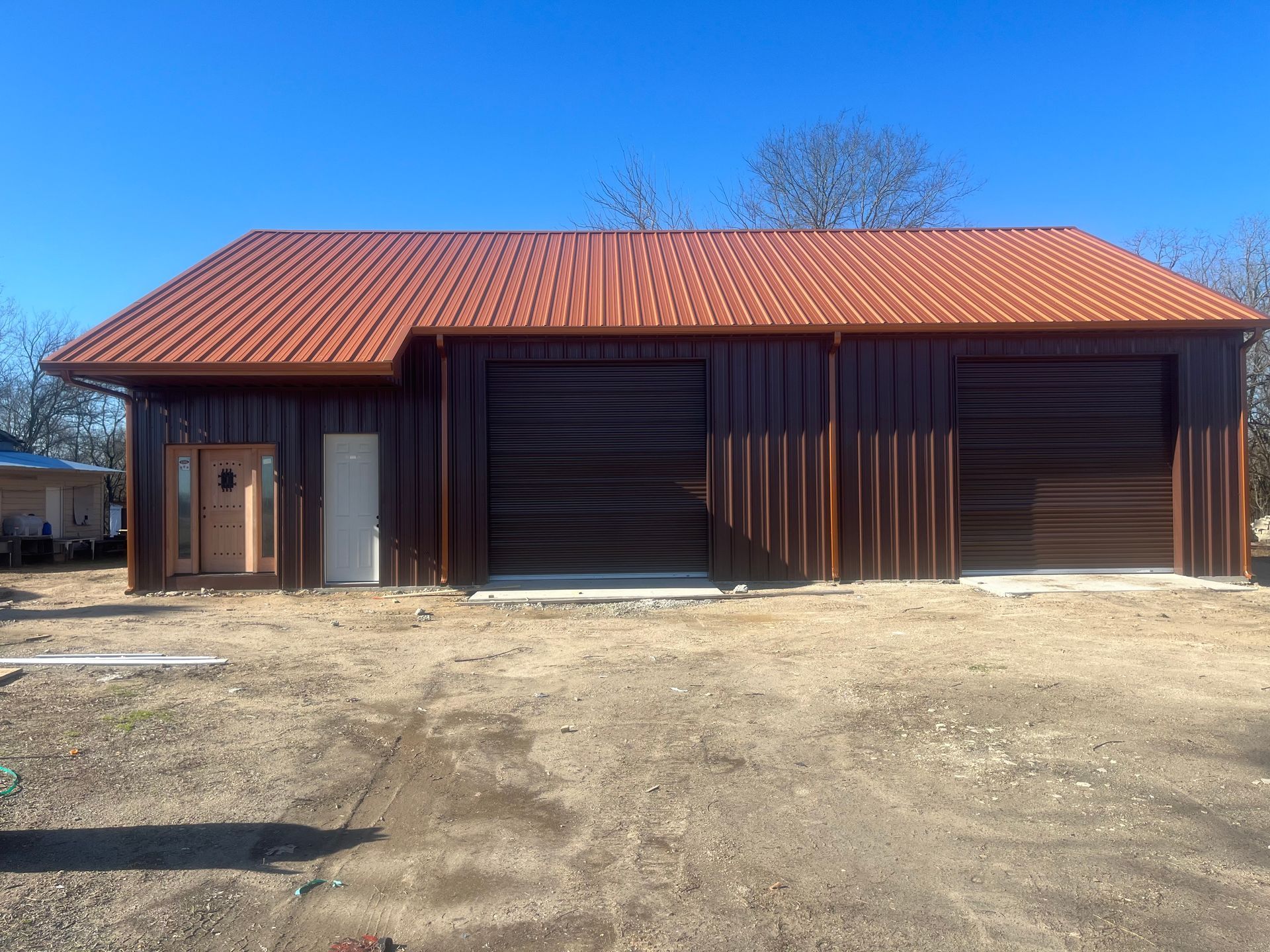 A large brown building with a red roof is sitting in the middle of a dirt field.