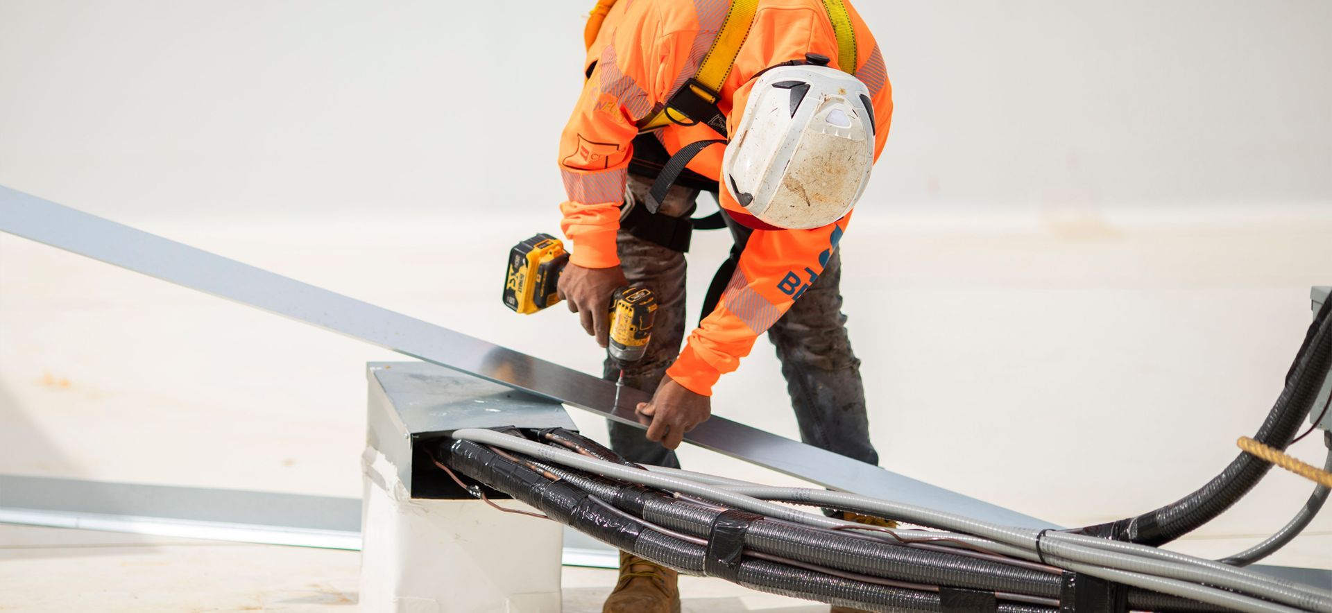 Worker in orange safety gear cutting a black cable on a rooftop or industrial surface