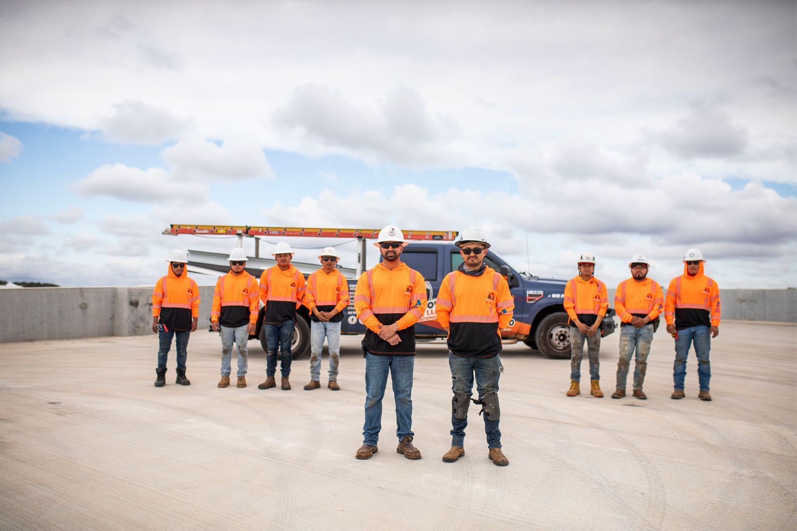 Workers in orange safety jackets stand on a rooftop under a cloudy sky.