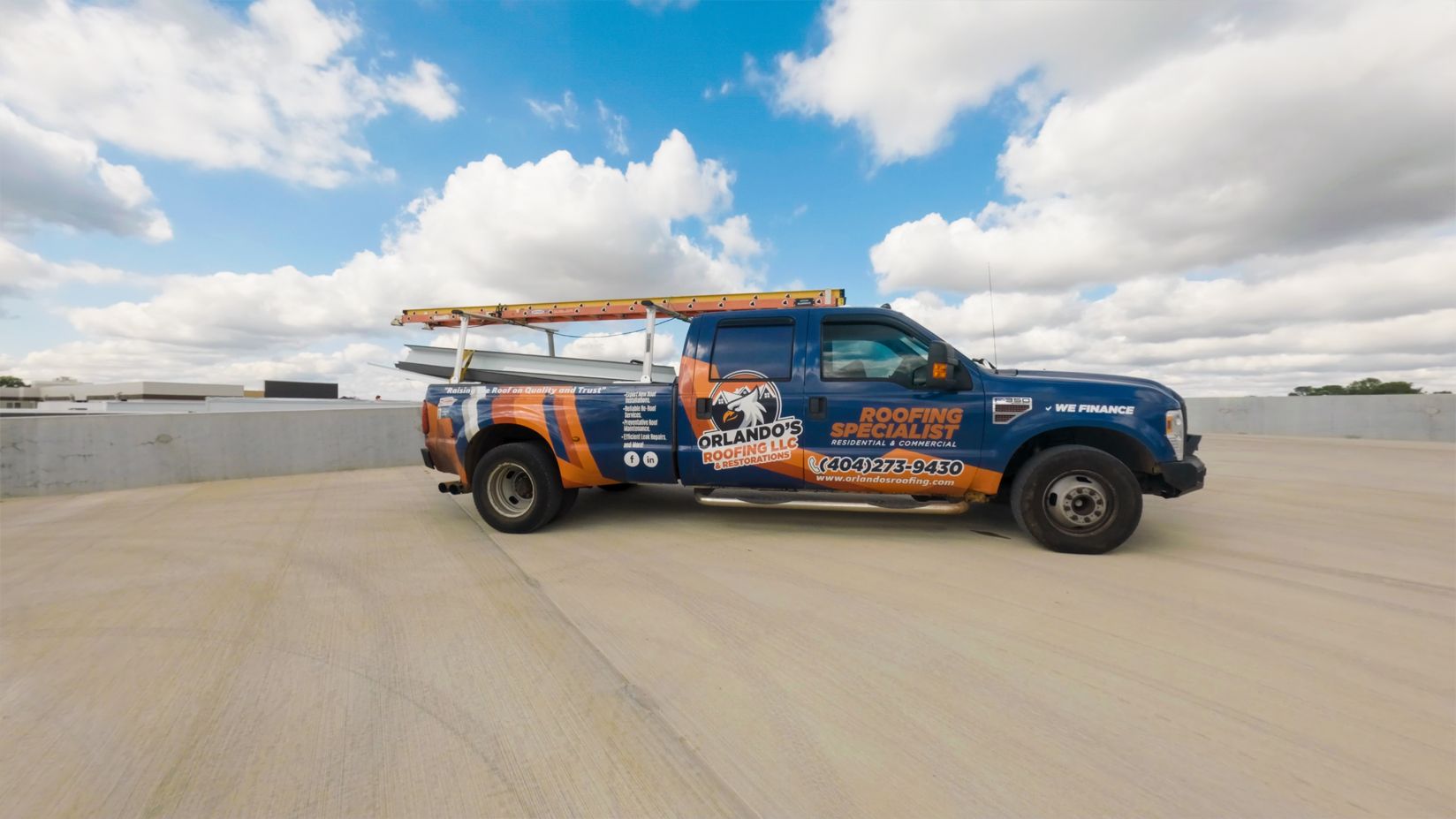 Blue-and-orange utility truck parked on a rooftop under a cloudy sky