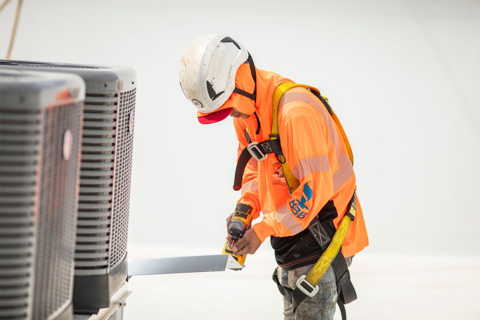 Worker in orange safety gear inspecting outdoor HVAC units with a handheld tool.