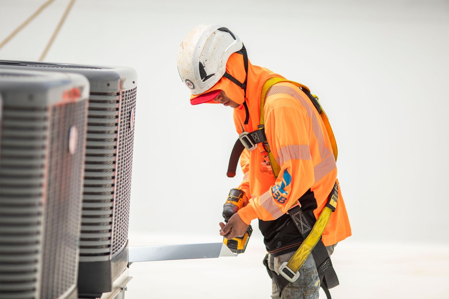 Worker in orange safety gear servicing an outdoor HVAC unit.