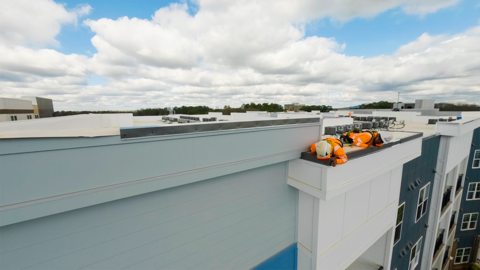 Workers on a rooftop beside orange equipment atop a modern building under a cloudy sky