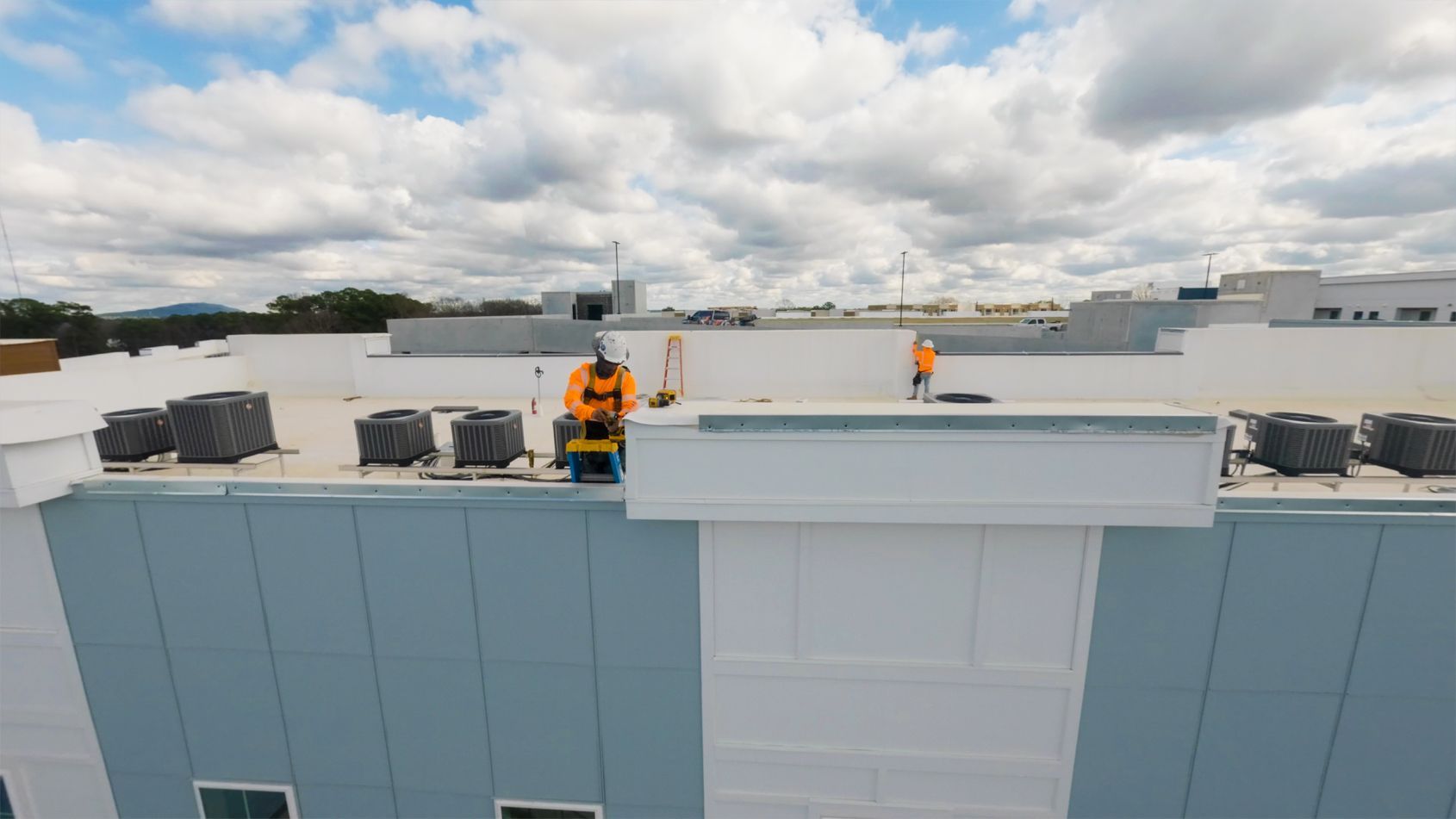 Workers on a flat rooftop near HVAC units under a cloudy sky