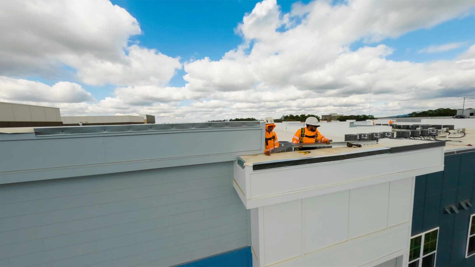 Roofing crew working on a flat rooftop under a cloudy blue sky