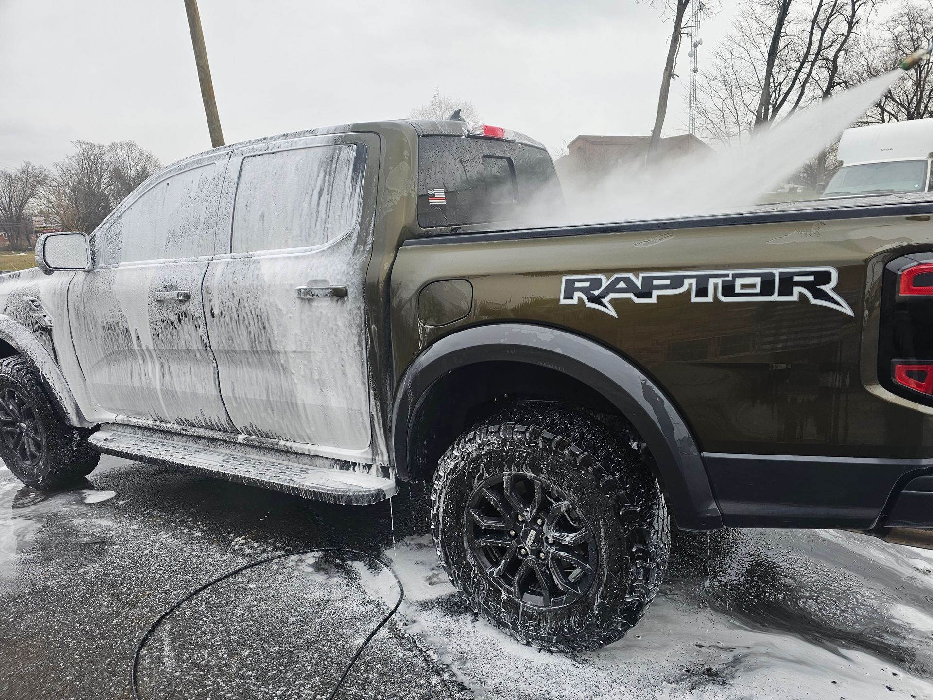 Green Ford Raptor truck covered in white foam being pressure washed outside.