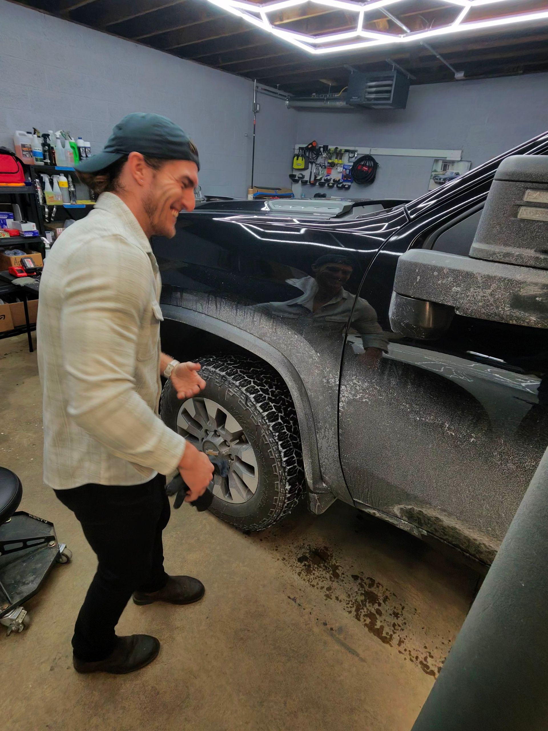 Man spraying a black truck with a white substance in a garage. He is smiling and excited.