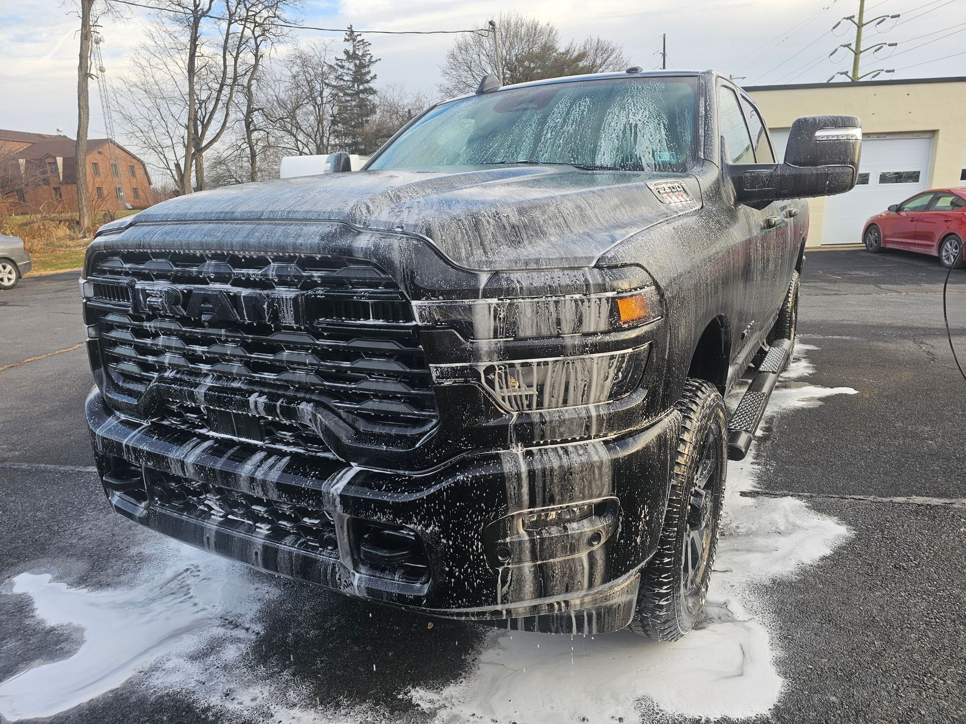Black pickup truck covered in white foam, being washed outside a building.