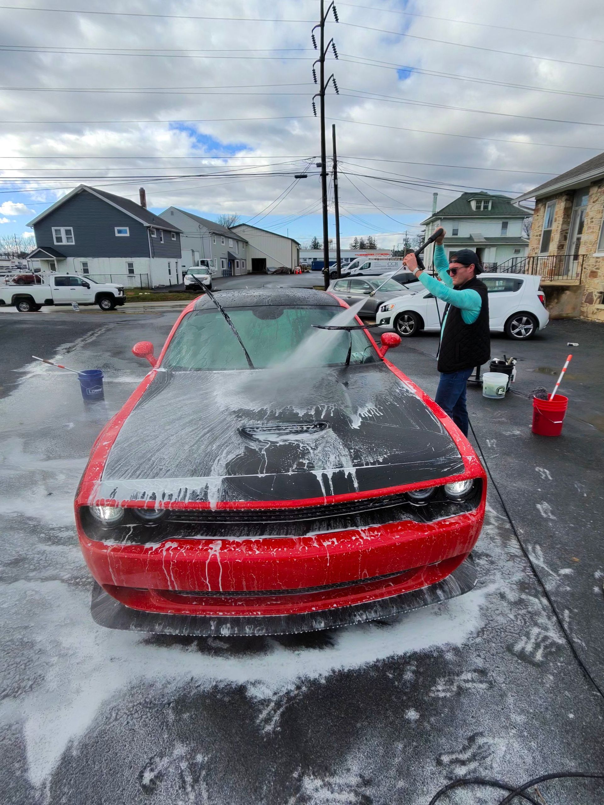 Person washing a red Dodge Challenger with soap in an outdoor setting.