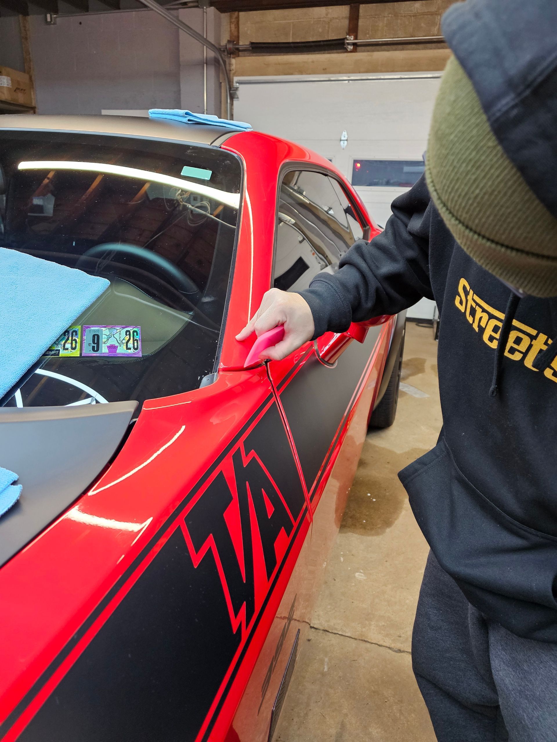 Person applying vinyl decal on red car with black stripes.