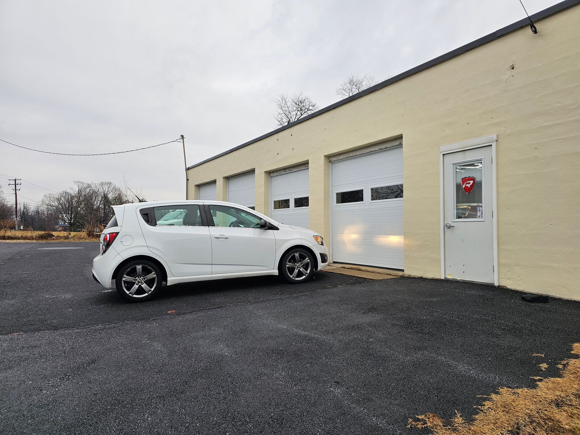 White car parked outside a beige garage with three bays and a white door. Cloudy sky.