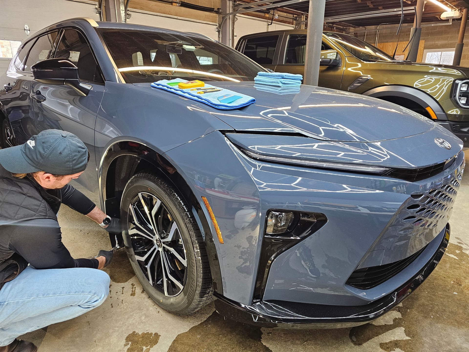 Person washes a gray electric vehicle at a car wash. A green truck is in the background.