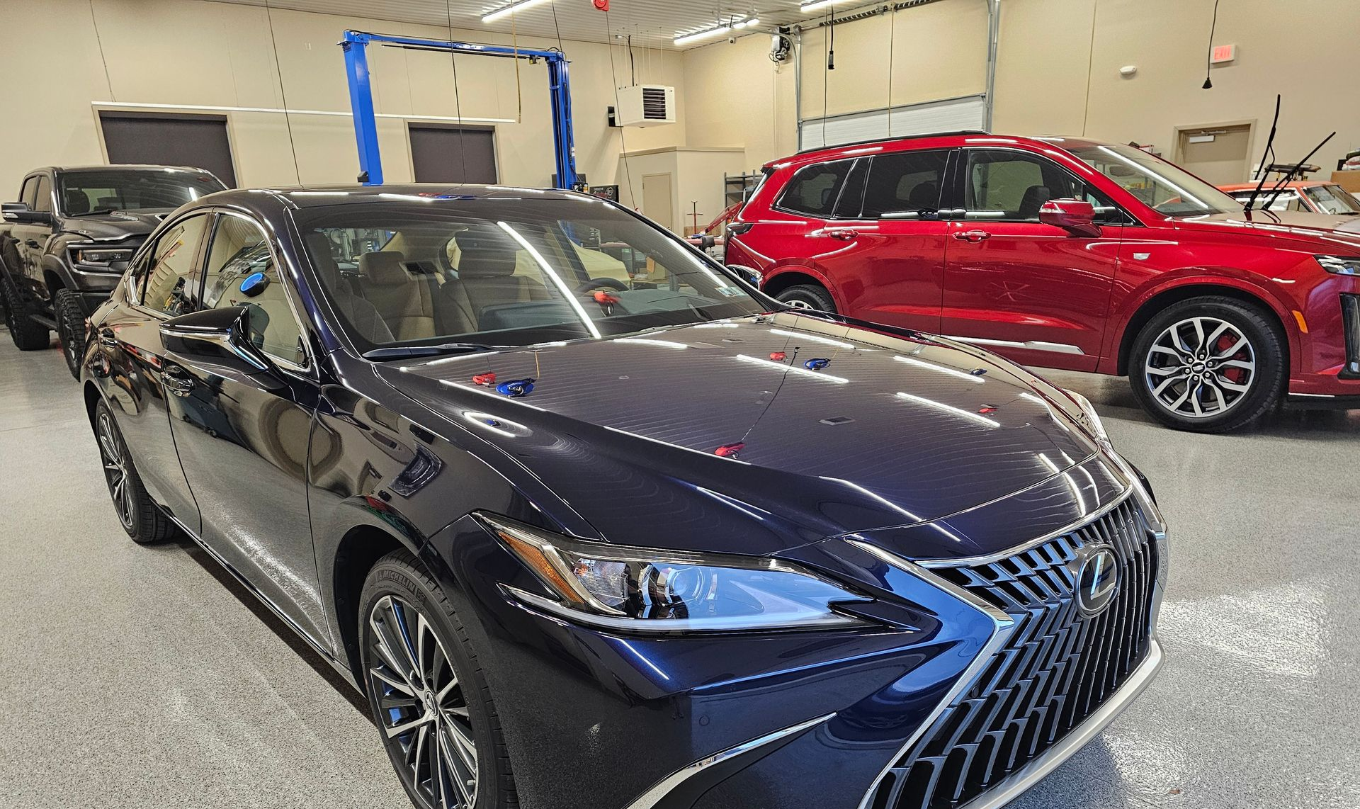 A dark blue Lexus sedan parked in a car dealership, with a red SUV in the background.