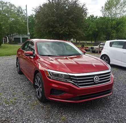 Red Volkswagen sedan parked on gravel in front of a building.
