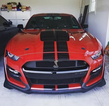 Red Ford Mustang Shelby GT500 with black racing stripes parked inside a garage.