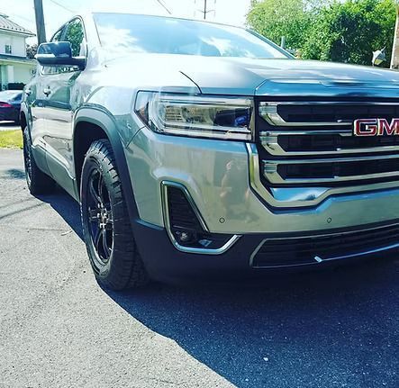 Silver GMC Acadia SUV parked on a paved road, front view, sunny day.