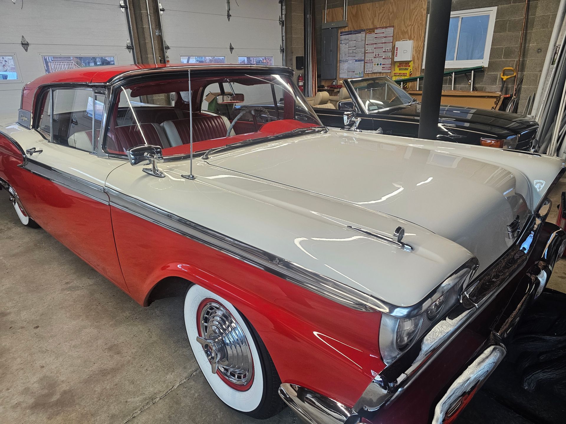 Red and white vintage car parked inside a garage. Whitewall tires, chrome trim.