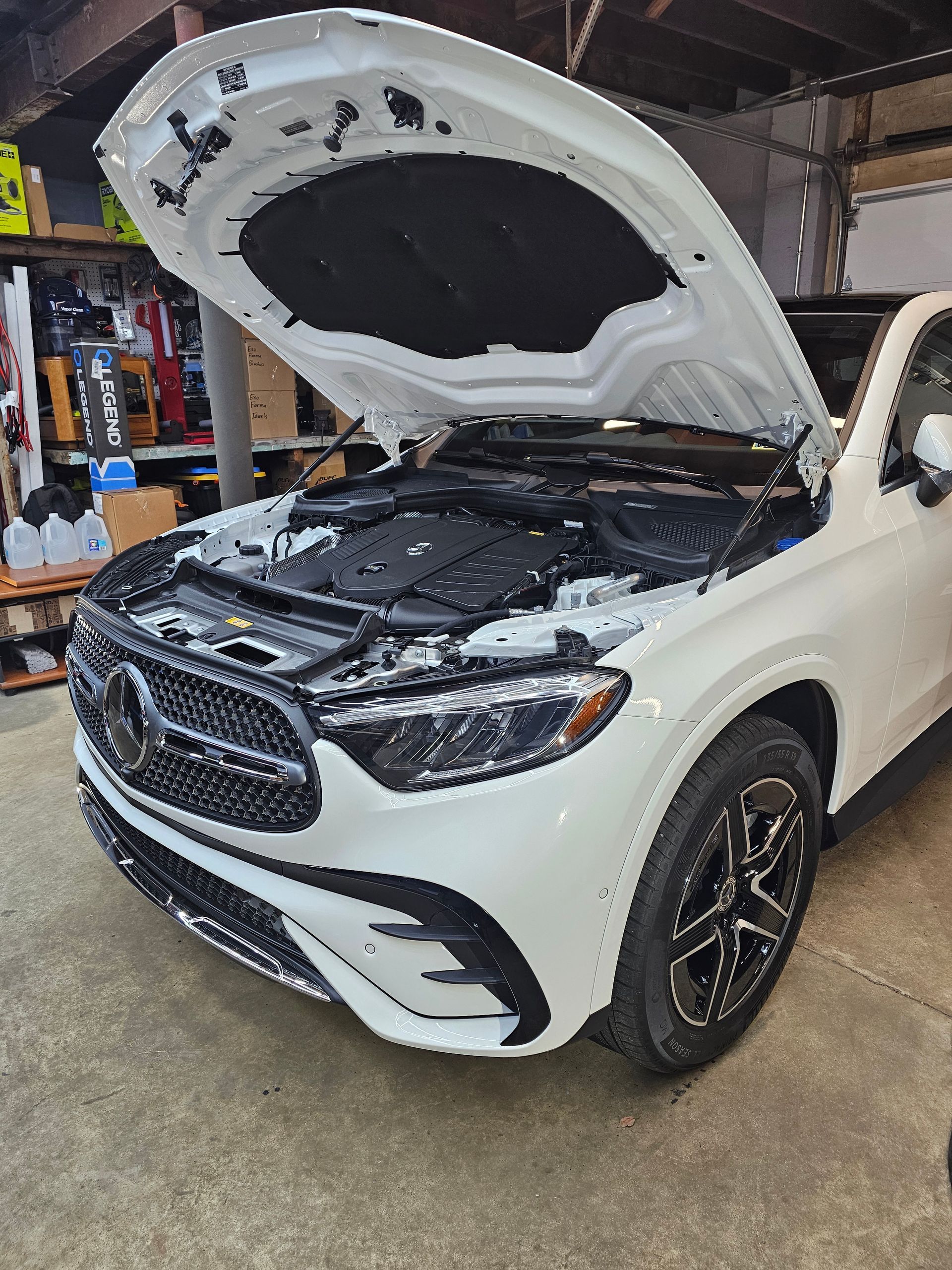 White Mercedes SUV with hood open, in a garage.