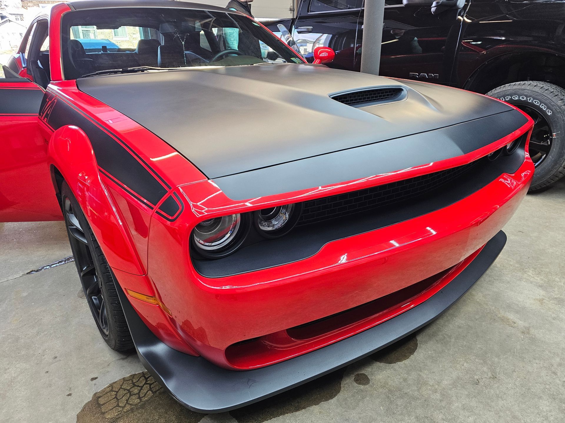 Red Dodge Challenger with black hood and racing stripe; front view, parked.