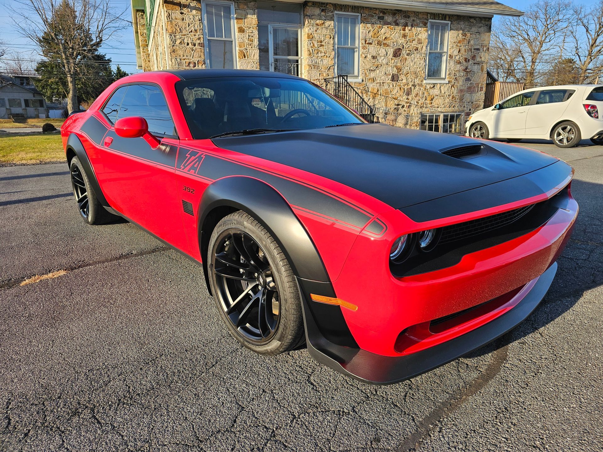 Red and black Dodge Challenger with black wheels parked in front of a stone building.