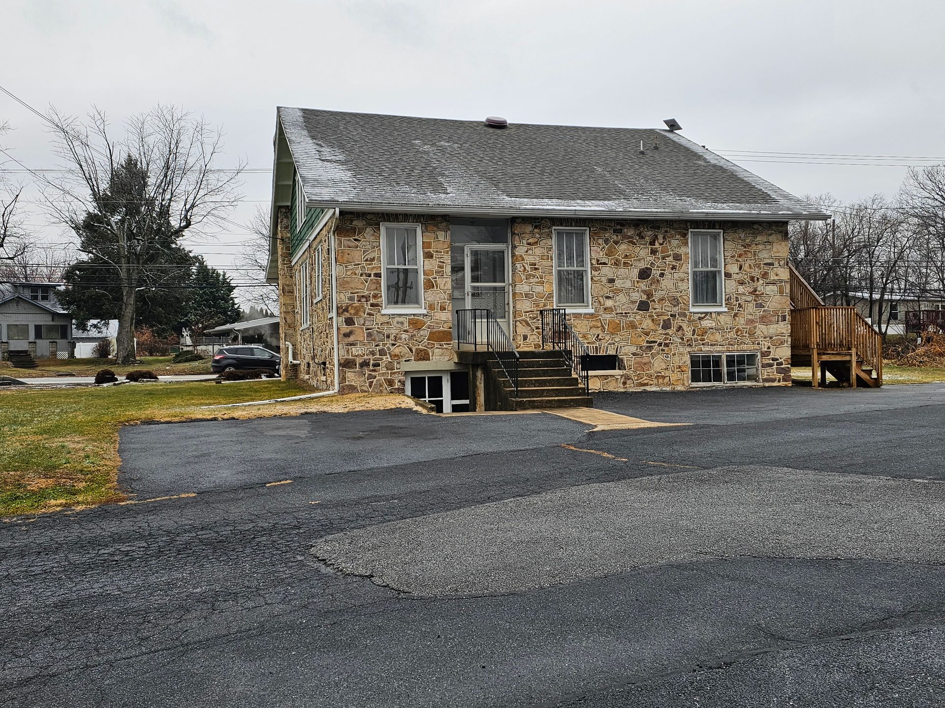 Stone house with dark roof and small front porch, on a gravel driveway, overcast day.