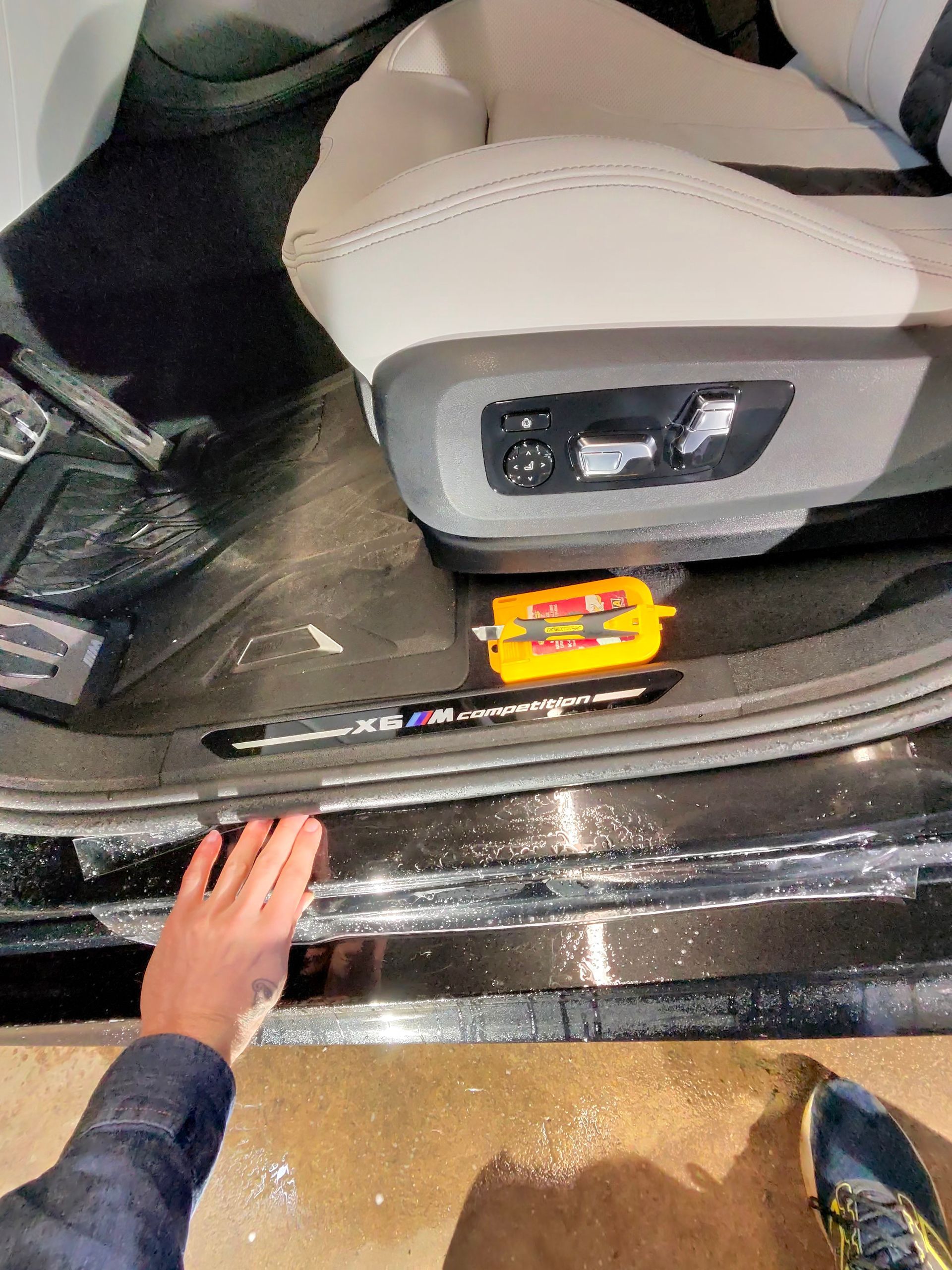 Hand reaching towards a car's interior with tools on the floor: a pen and a small yellow tool case.