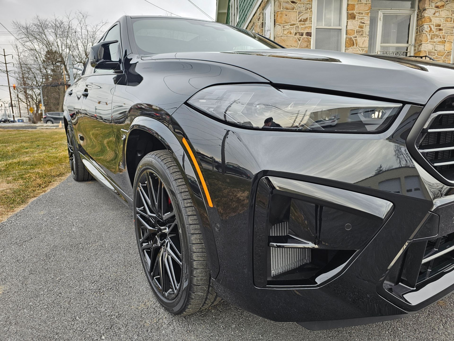 Black BMW SUV parked on a paved driveway with black rims, cloudy sky, brick building in background.