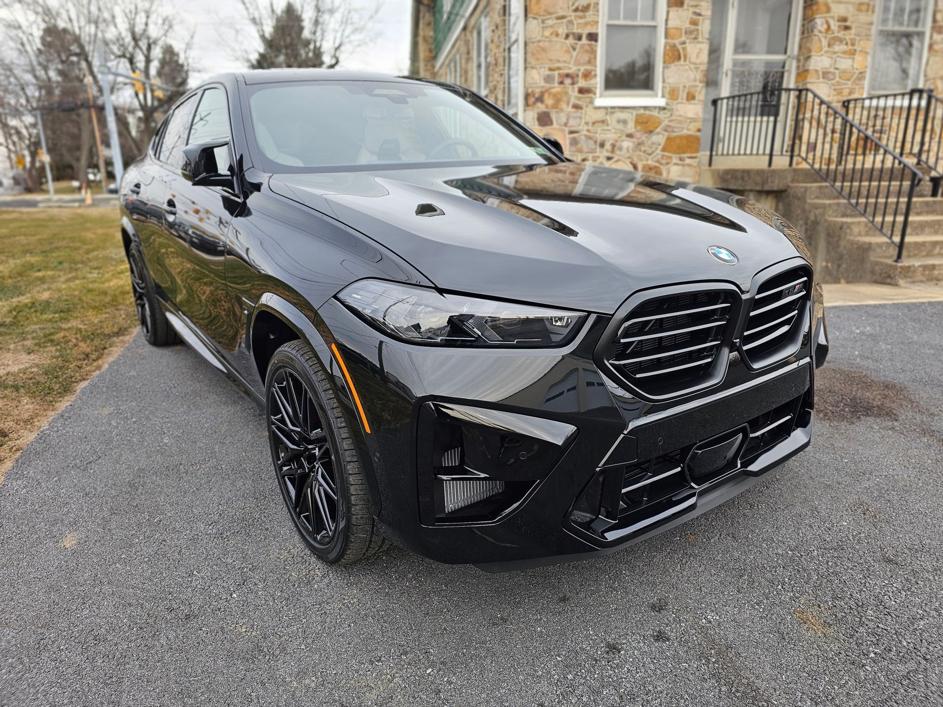 Black BMW X6 SUV parked on gravel driveway in front of a brick building.