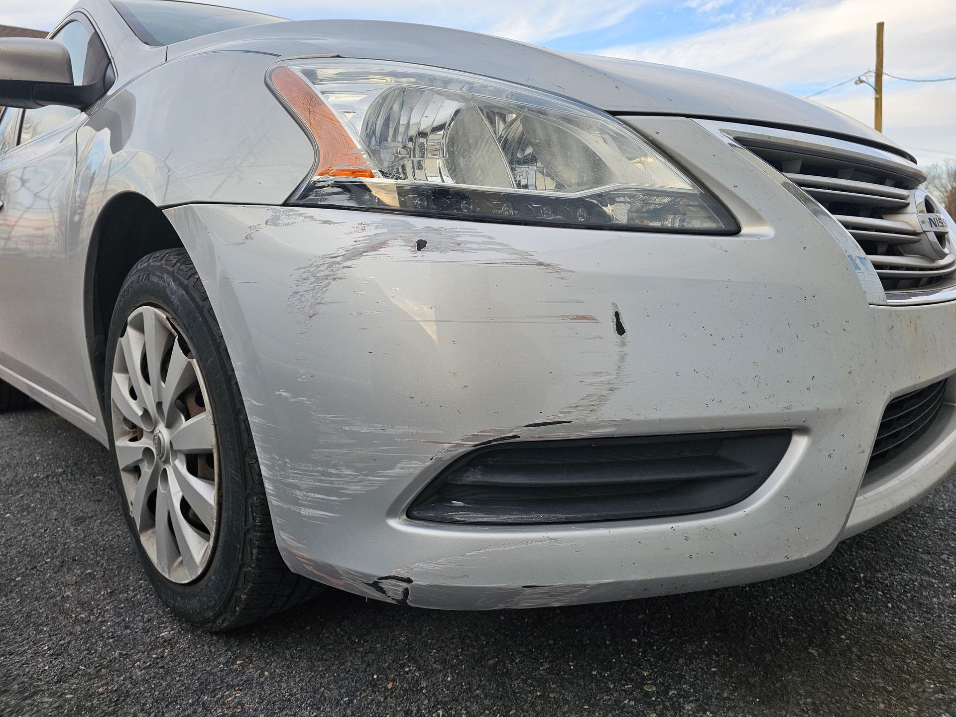 Silver car front bumper with scratches and damage.