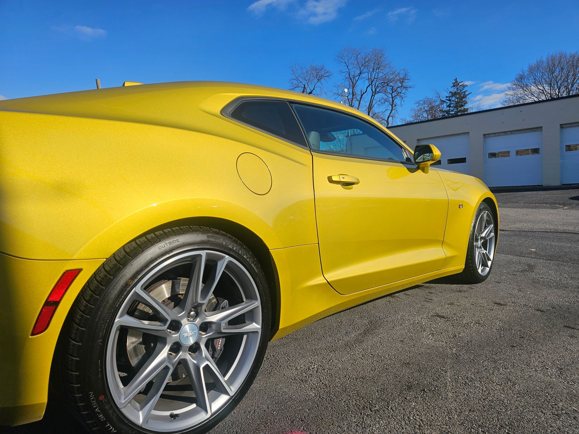 Yellow sports car parked on gravel. Sunny day with a blue sky.
