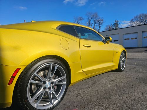 Yellow sports car parked on gravel. Sunny day with a blue sky.