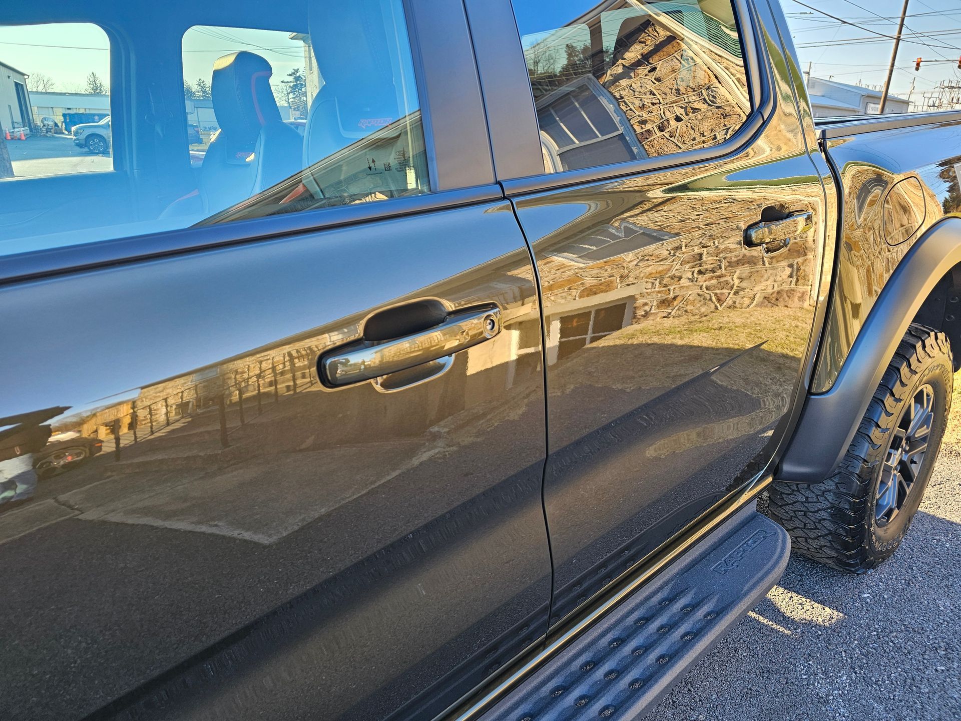 Black pickup truck door and side with a black running board, handle, and tire.