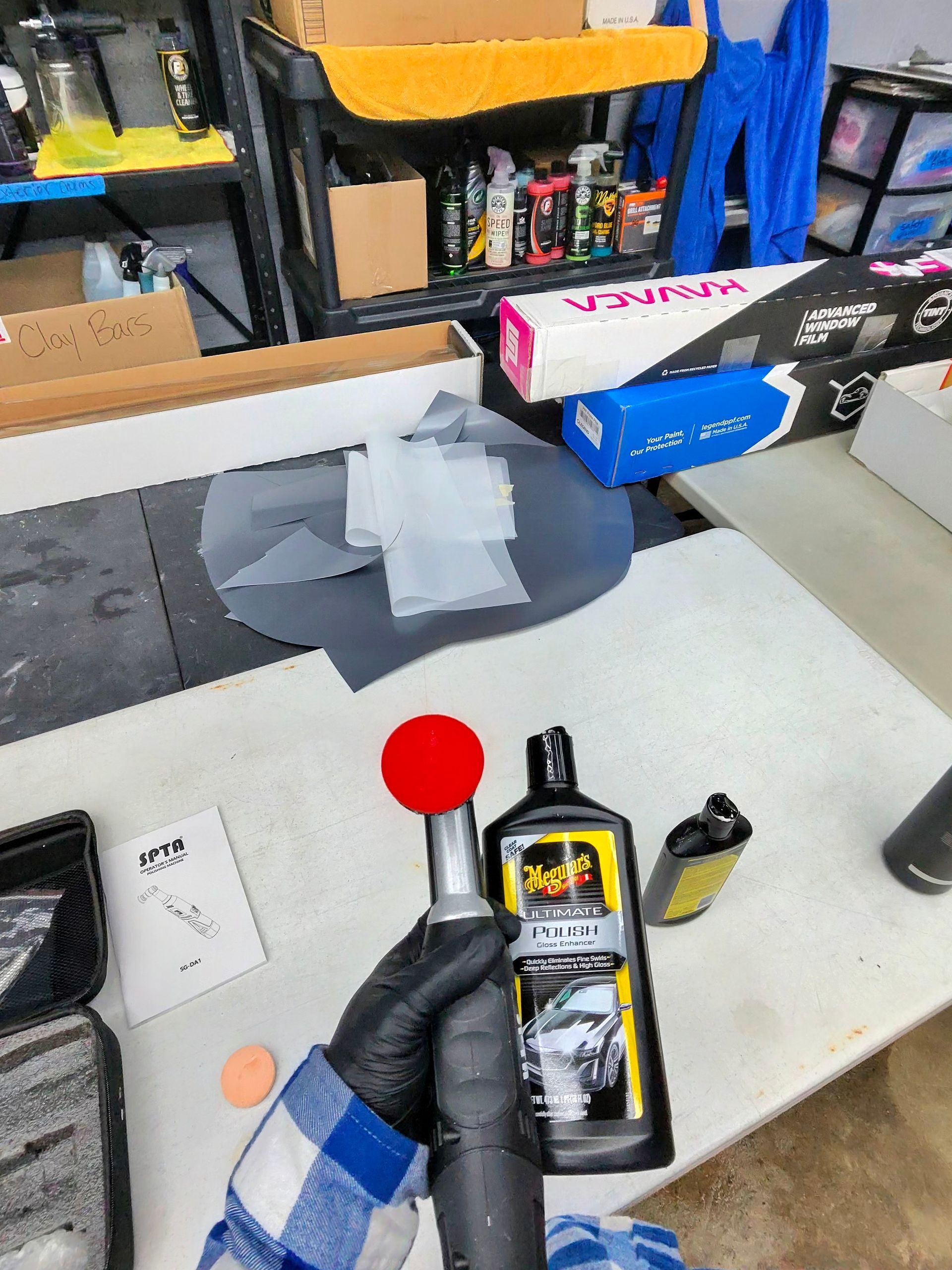 Person holding a polisher, detailer products, work surface, and various car cleaning supplies.