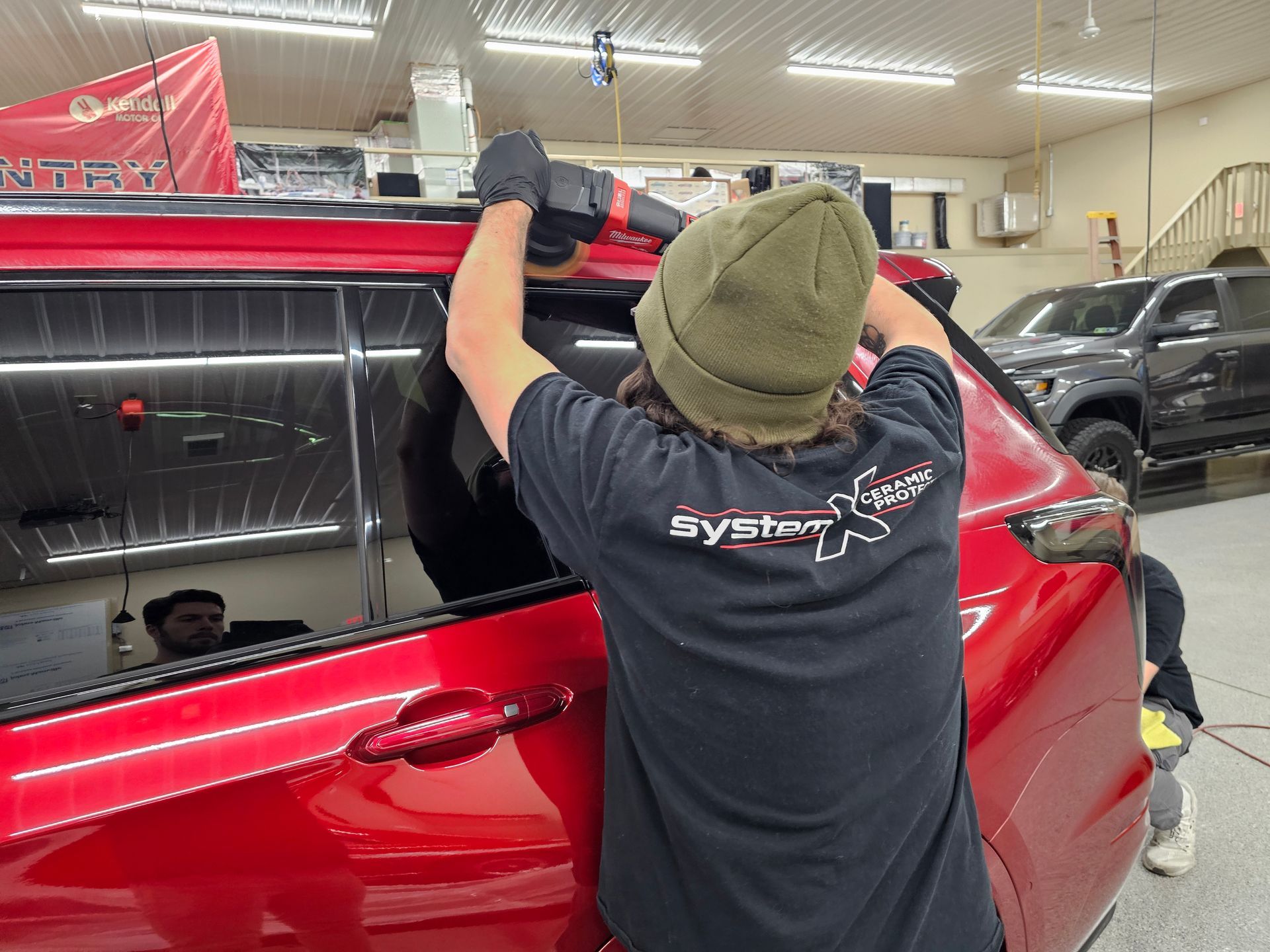 Person using a power tool on a red car window. Inside a shop.