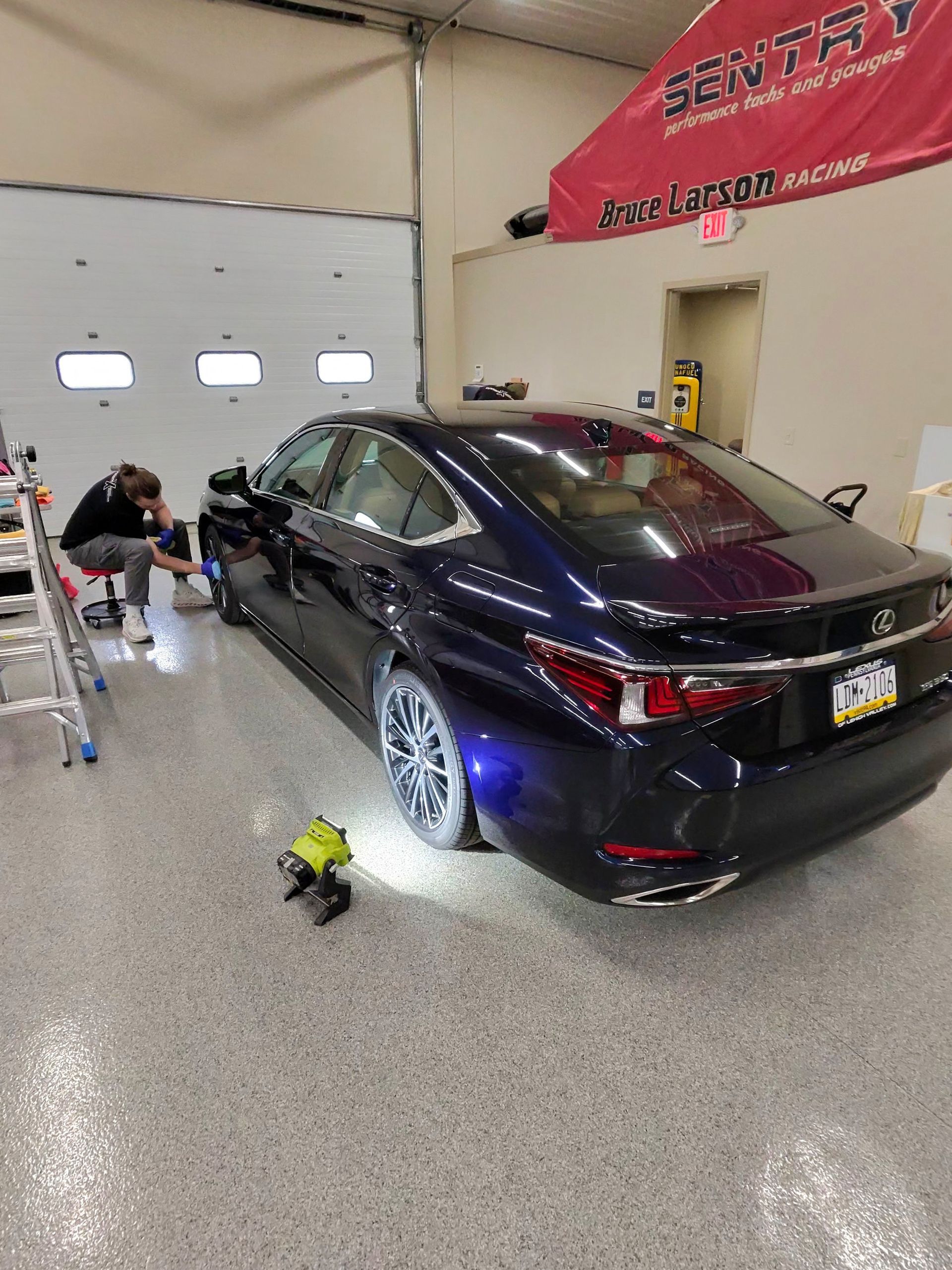 A person working on a dark blue Lexus in a garage with a light shining on the car's tire.