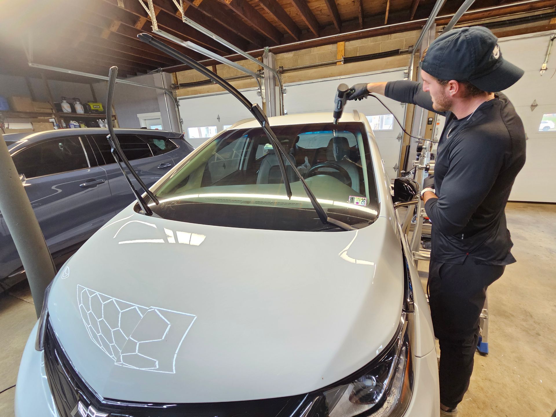 Man cleaning the windshield of a white car inside a garage.