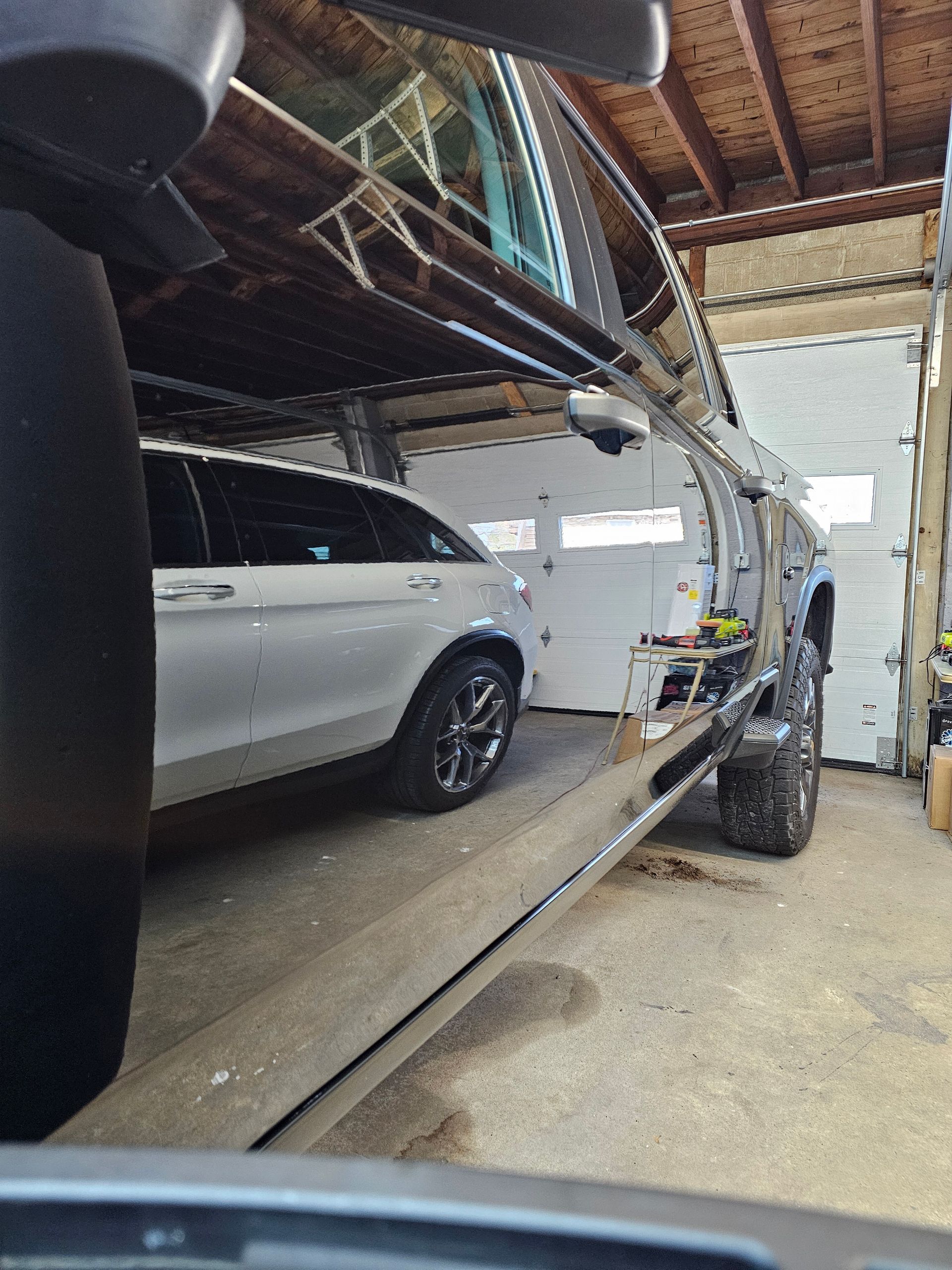 Silver car parked in a garage with a partially open door; a large truck is visible.