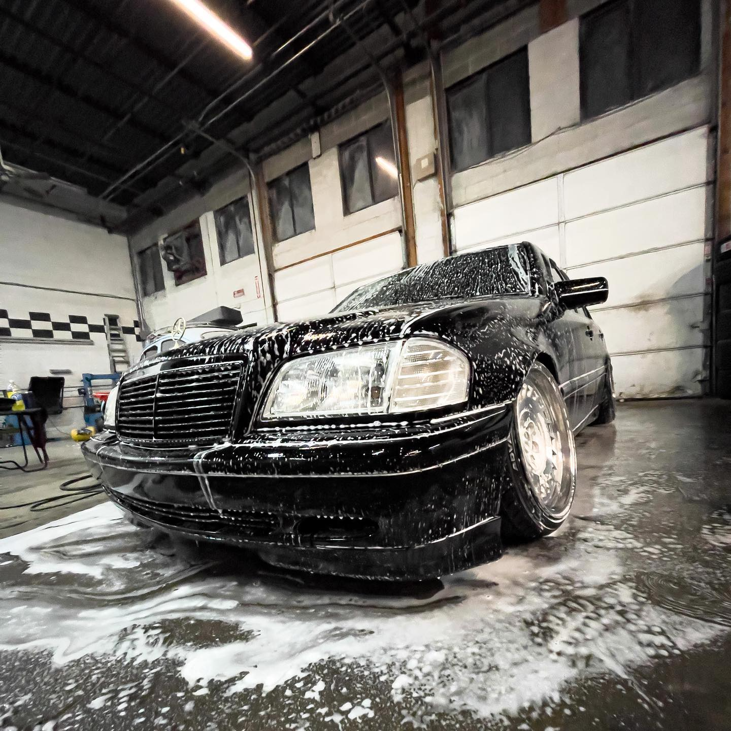 Black car covered in soap suds inside a garage, tires angled, being washed.