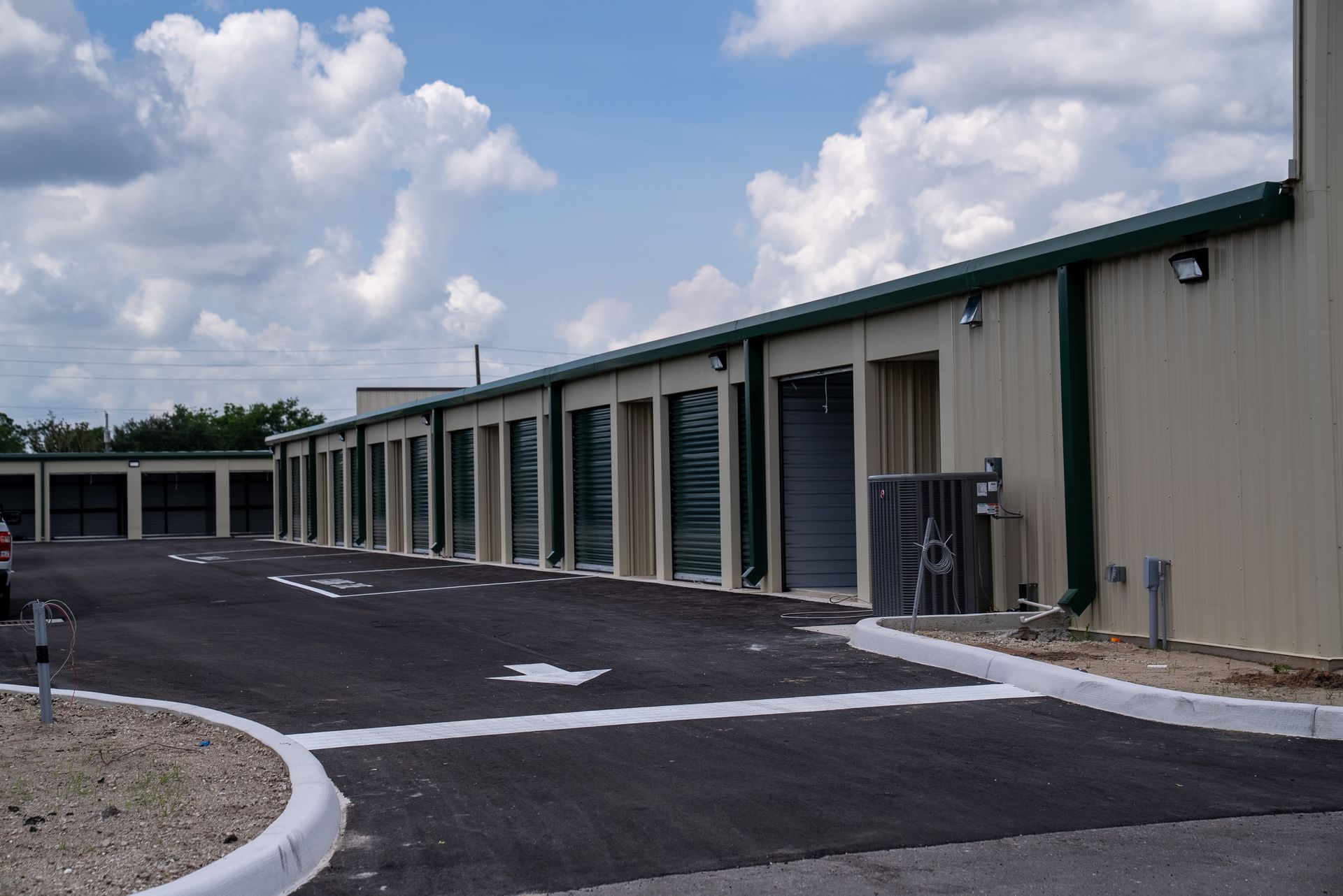 Row of beige storage units along a paved driveway under a cloudy sky