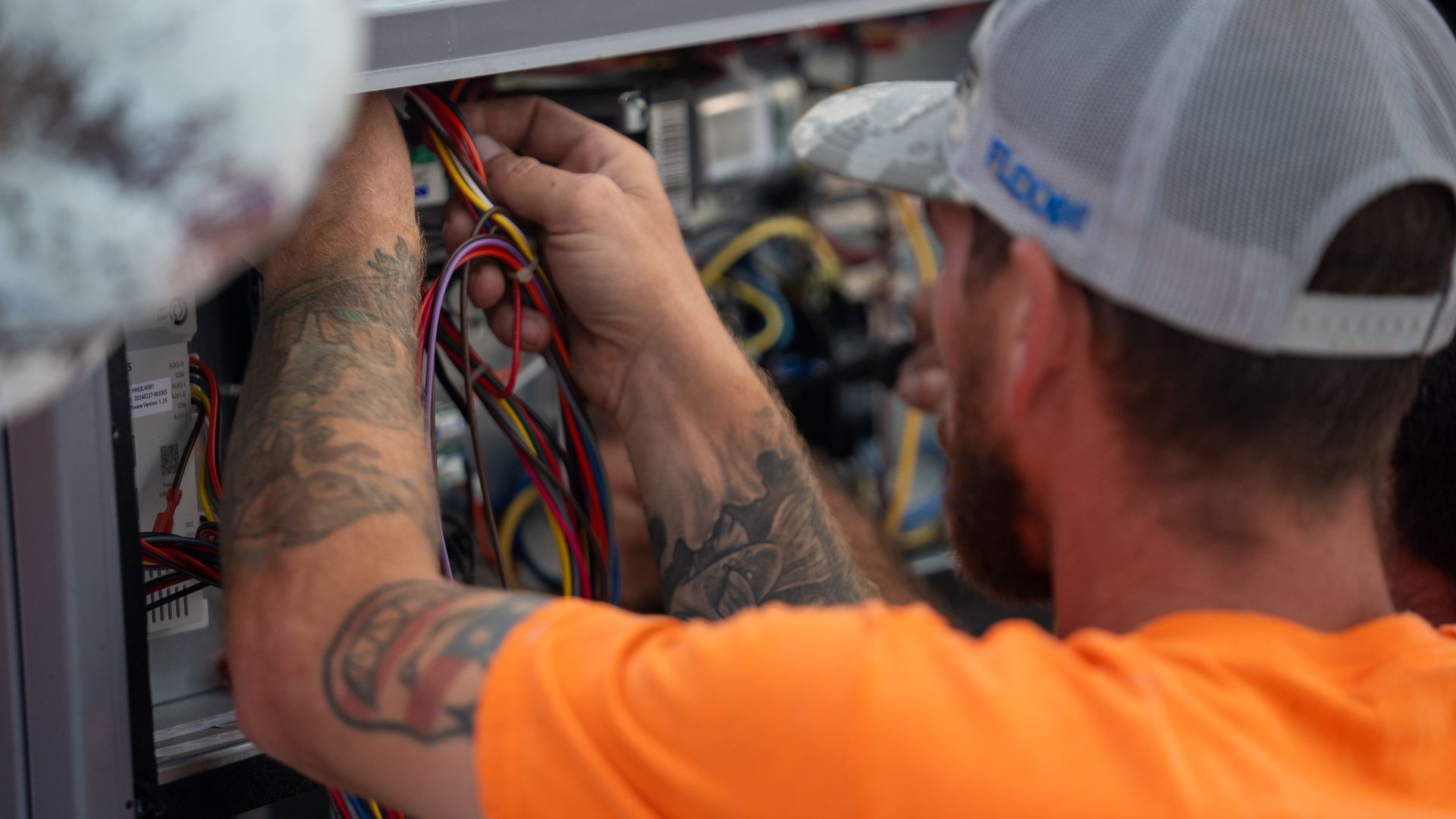 Electrician wiring an electrical panel with colorful cables in a utility box.
