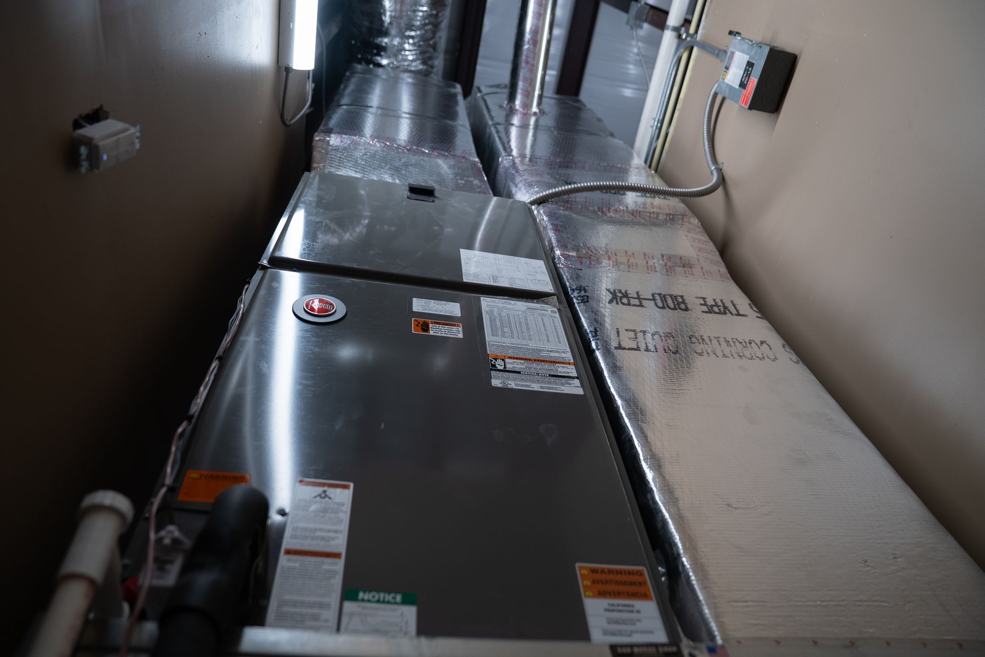 Metal HVAC ductwork in a narrow utility hallway, with reflective panels and wall-mounted controls
