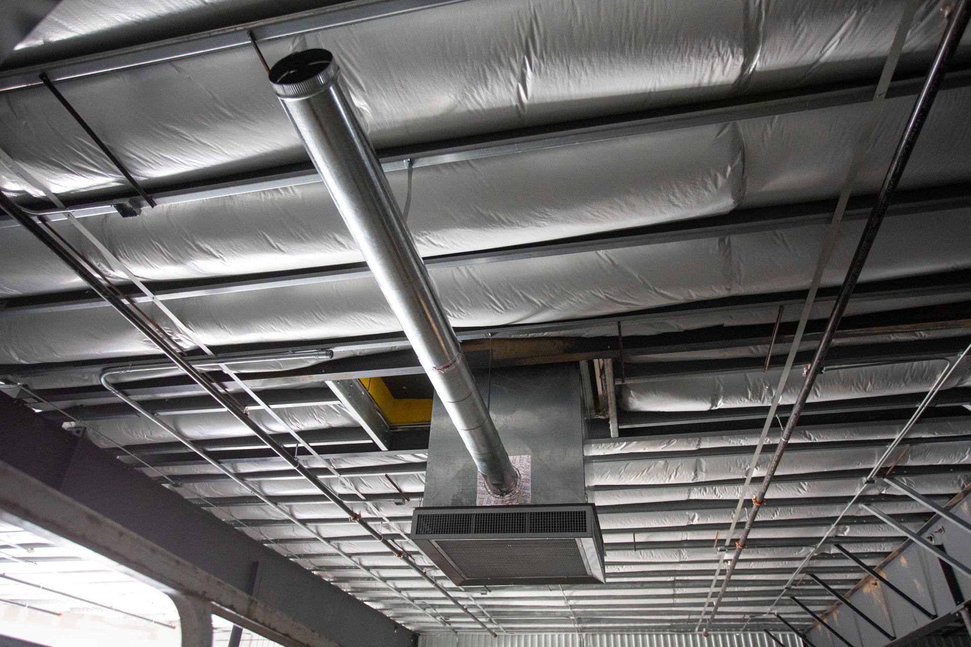 Industrial ceiling with exposed silver ductwork and metal framing in a warehouse-like interior