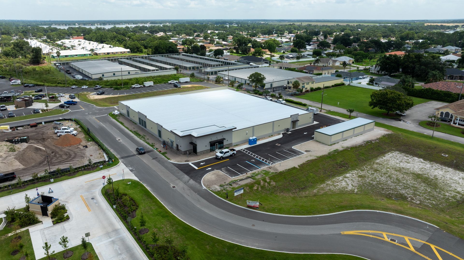 Aerial view of a large white warehouse beside a curved road in a suburban industrial area.